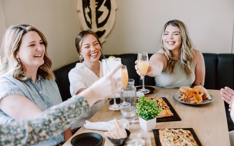 a group of women sitting at a table with food and drinks